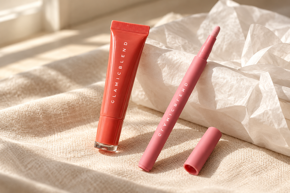 A coral lip glaze tube and a pink lip contour pen on cream linen beside folded white tissue paper