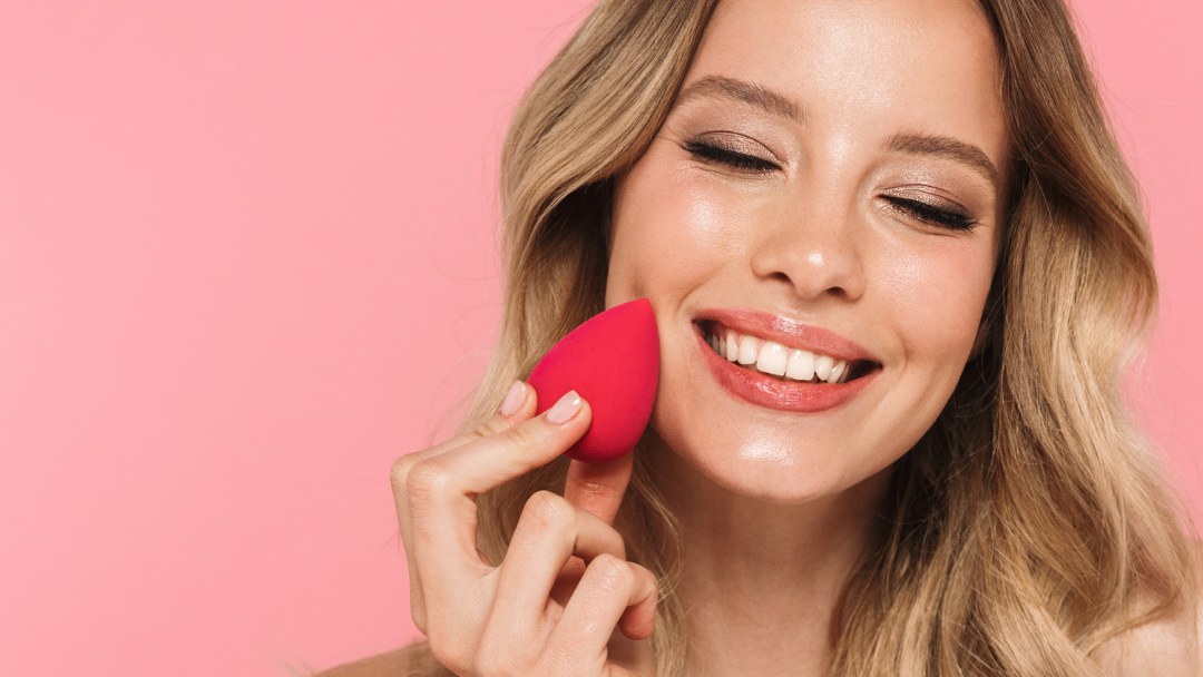 Smiling woman blending makeup with a pink sponge
